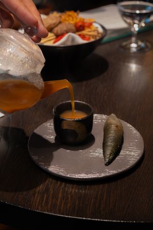 Orange sauce being poured over a dark-colored dish on a slate plate.