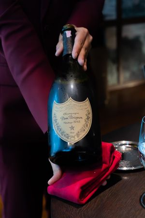 Champagne bottle being opened with a red cloth in dim lighting.