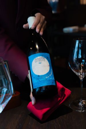 A blue wine bottle being poured in a dimly lit setting with wine glasses visible.