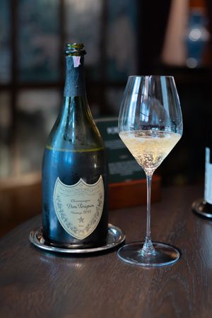 Bottle of Dom Perignon champagne displayed next to an empty wine glass on a wooden table.