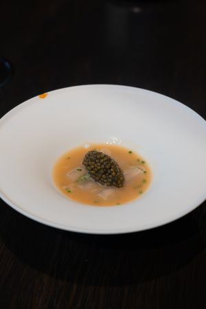 A white plate with caviar and broth served in an elegant minimalist presentation.