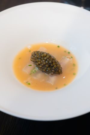 Caviar served in an orange-tinted broth on a white plate in an elegant presentation.