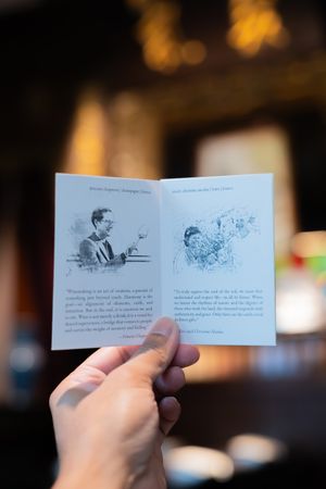 A hand holds a series of small illustrated story cards or pages against a dark blurred background.