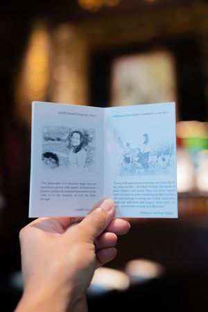 Small illustrated booklet or menu being held open to show sketched drawings.
