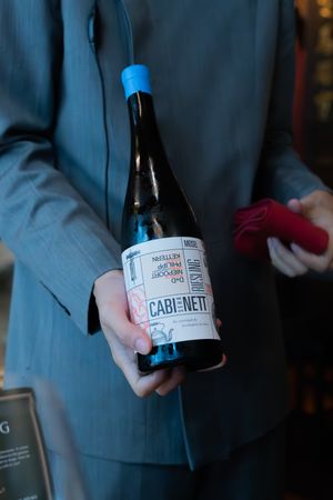 Hand holding a bottle of Cabernet wine against a dark background.