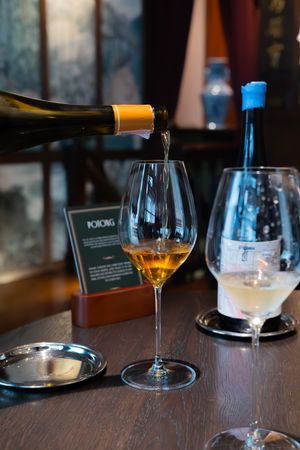 Wine glasses filled with golden liquid sit on a dark wooden table in a restaurant setting.
