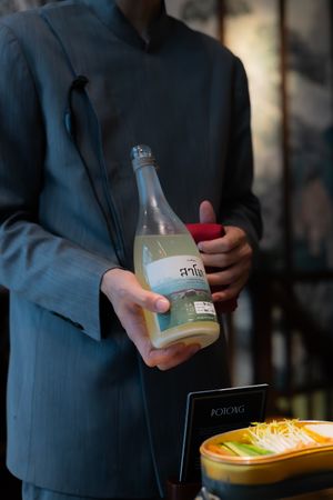 Someone in a dark suit pours a clear beverage from a glass bottle at an elegant dining setting.
