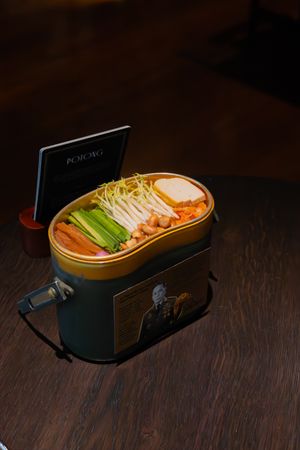 A stylish bento box lunch with fresh vegetables and garnishes sits atop a dark wooden surface.