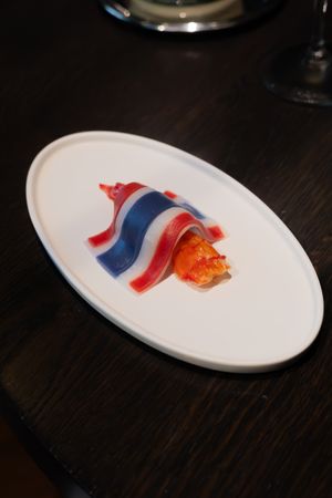 Red and blue artistic food presentation on white oval plates against a dark wooden surface.