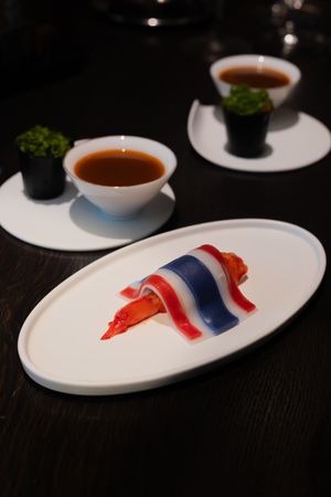 White oval plates with red and blue artistic sauce designs and small bowls of dark sauce.