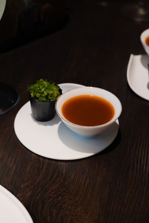 A white bowl of clear broth garnished with fresh herbs on a dark wooden table.