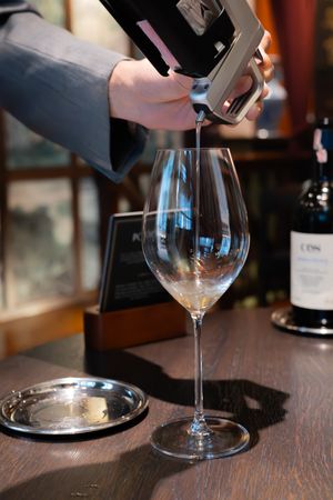 Wine being poured into an elegant crystal wine glass on a dark wooden table at a tasting event.