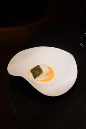 Artistic plating of orange sauce and garnish on a curved white ceramic dish.
