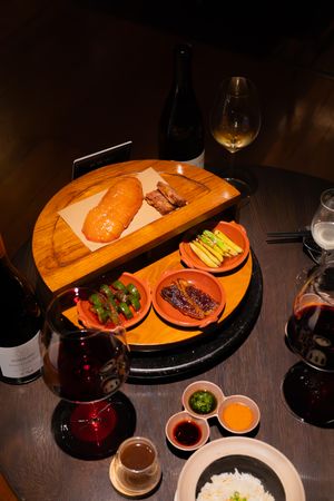 Wooden serving board with various dishes and wine glasses in a dimly lit restaurant setting.