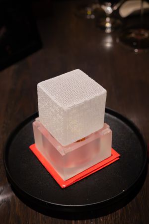 Illuminated translucent cube on a black plate with red lighting underneath creates dramatic presentation.