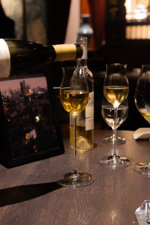 Wine glasses sit on a dark wooden table in a dimly lit restaurant setting with warm ambient lighting.