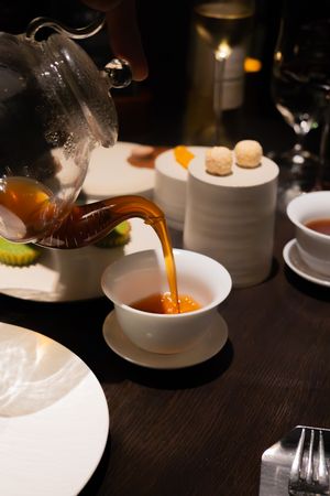 Hot liquid being poured into white ceramic bowls on dark wooden table.