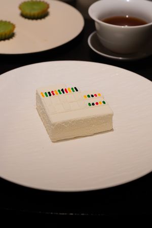 White plates arranged with colorful dot markers and thin slices of white food on a dark surface.
