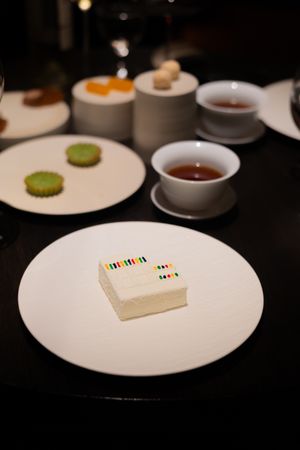 White plates with small decorative items arranged on a dark table in a fine dining setting.