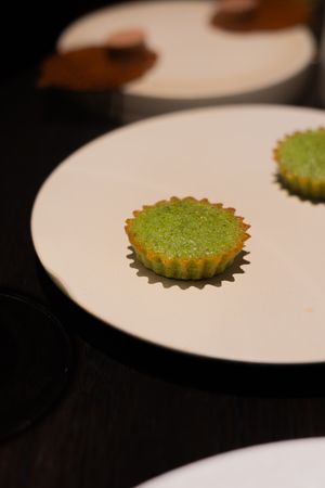 Small green matcha tart displayed on a white plate against a dark background.