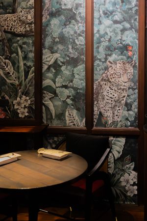 Restaurant interior with floral wallpaper featuring leopard prints and wooden tables.
