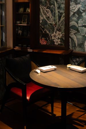 Restaurant interior with wooden tables and floral wallpaper in moody lighting creating an intimate atmosphere.