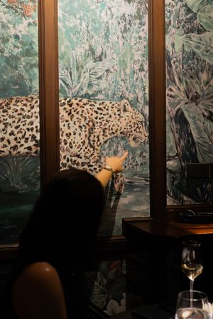 A decorative wall mural featuring a leopard in a tropical setting with wine glasses in the foreground.