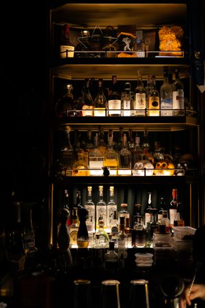Illuminated bar shelves display various liquor bottles and spirits in a moody, dark atmosphere.