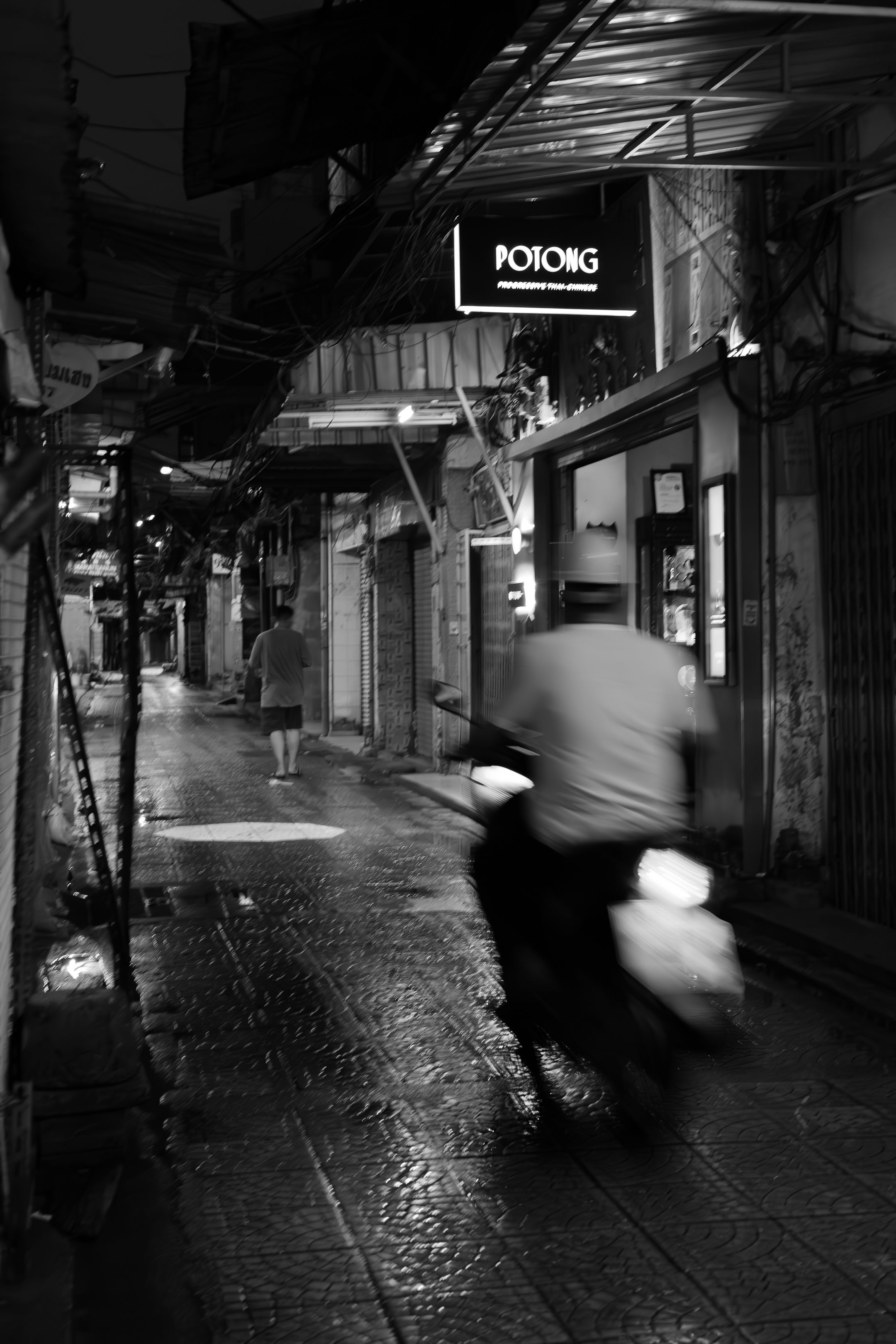 Blurred motion of people walking on a rainy cobblestone street at night with glowing lights reflecting off wet pavement.