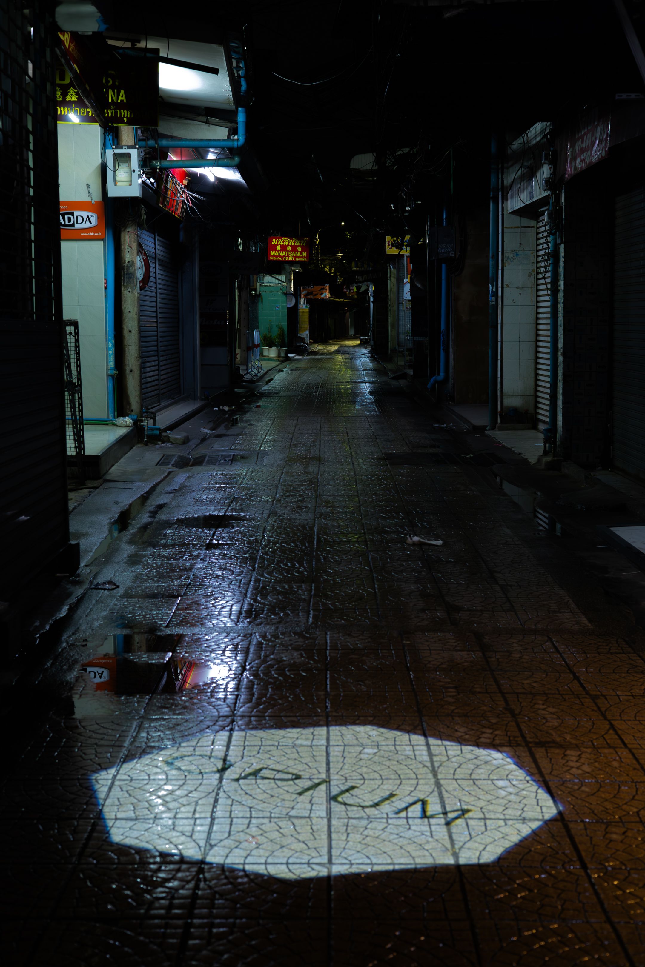 Dark wet alley in Japan with neon signs and a mysterious octagonal light pattern projected on the ground.