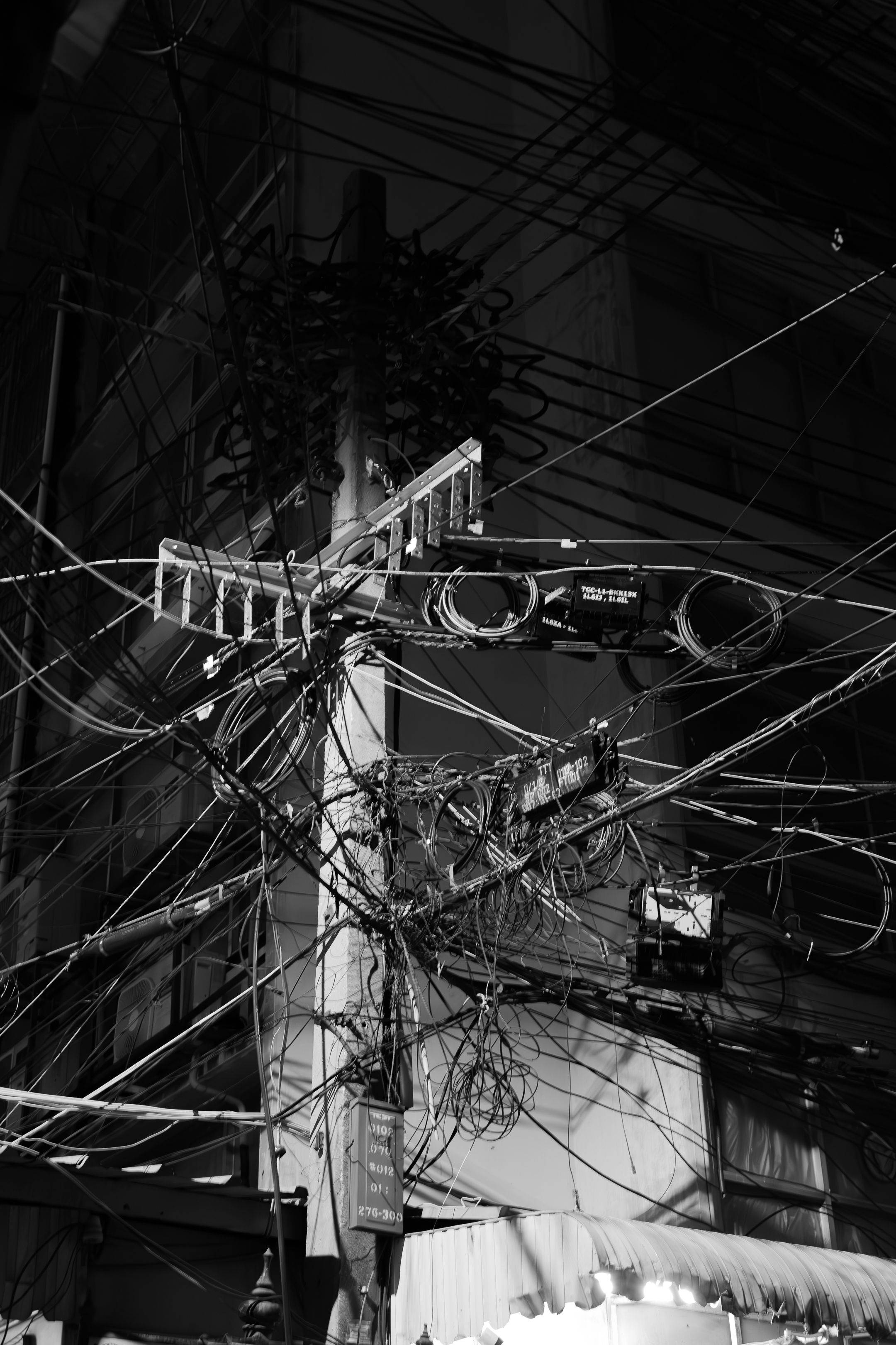 A chaotic tangle of electrical wires and cables connected to utility poles creates a complex web against a dark sky.