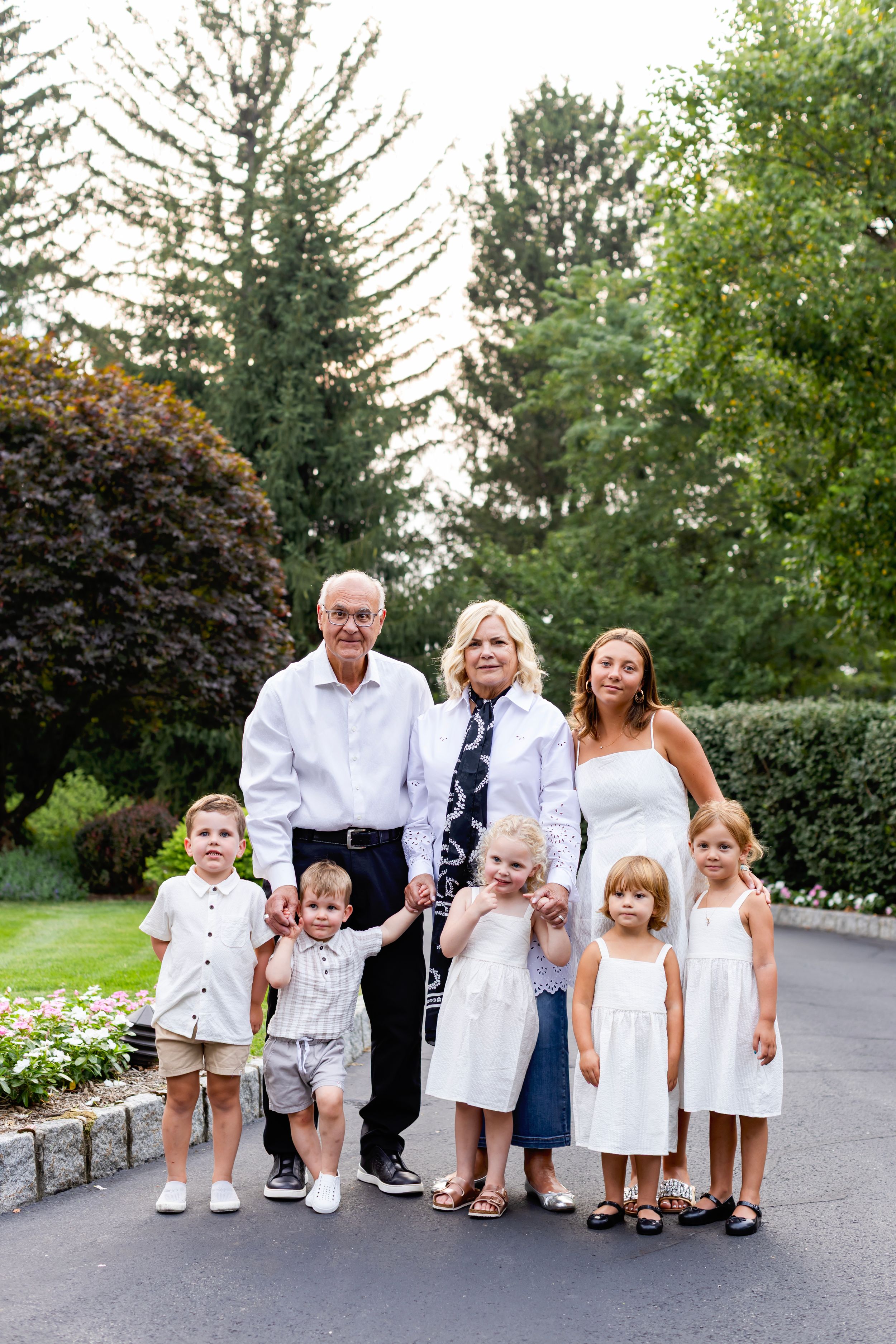A group of adults and children dressed in coordinating white and blue outfits pose together on a paved path outdoors.