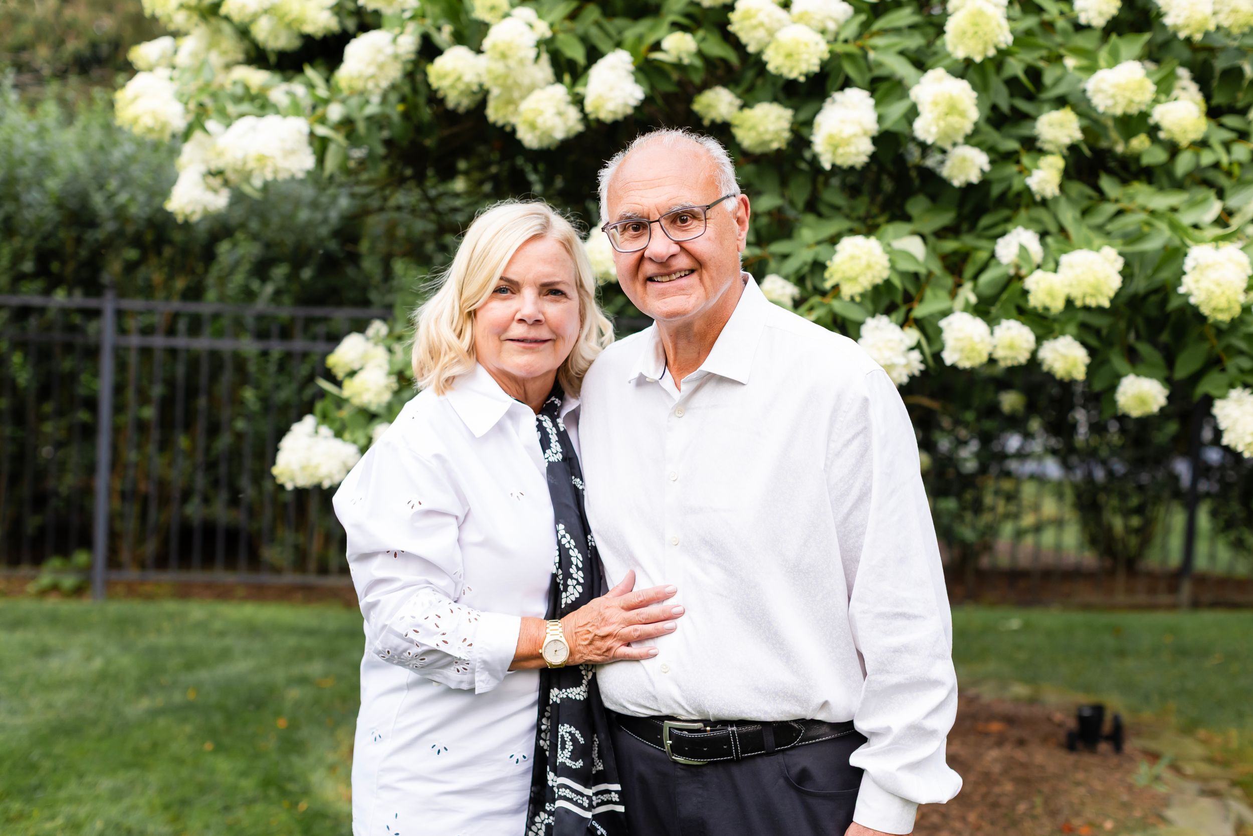 Group portrait taken outdoors with white hydrangea bushes blooming in the background.