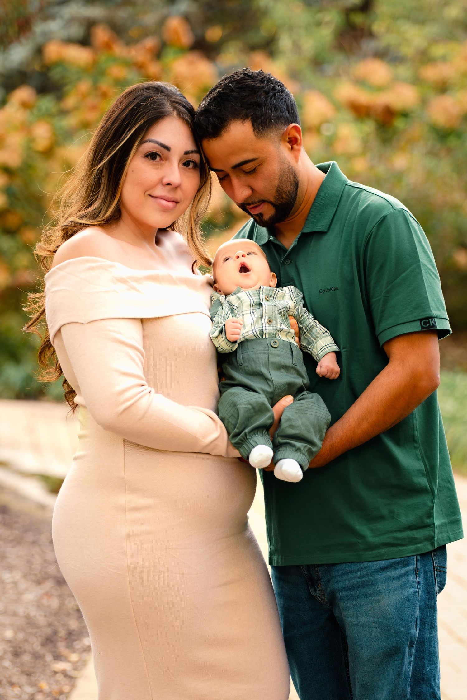 A family portrait outdoors featuring a couple with their baby in casual attire.