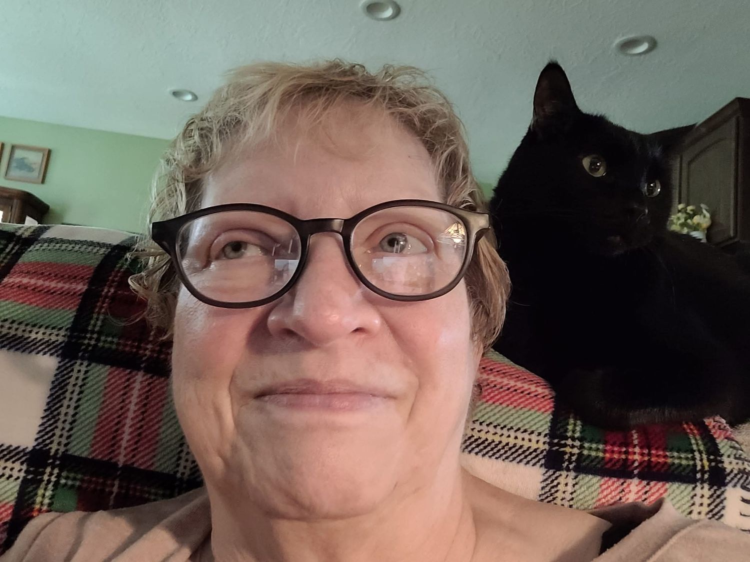 Woman with glasses taking a selfie with a black cat perched on her shoulder.