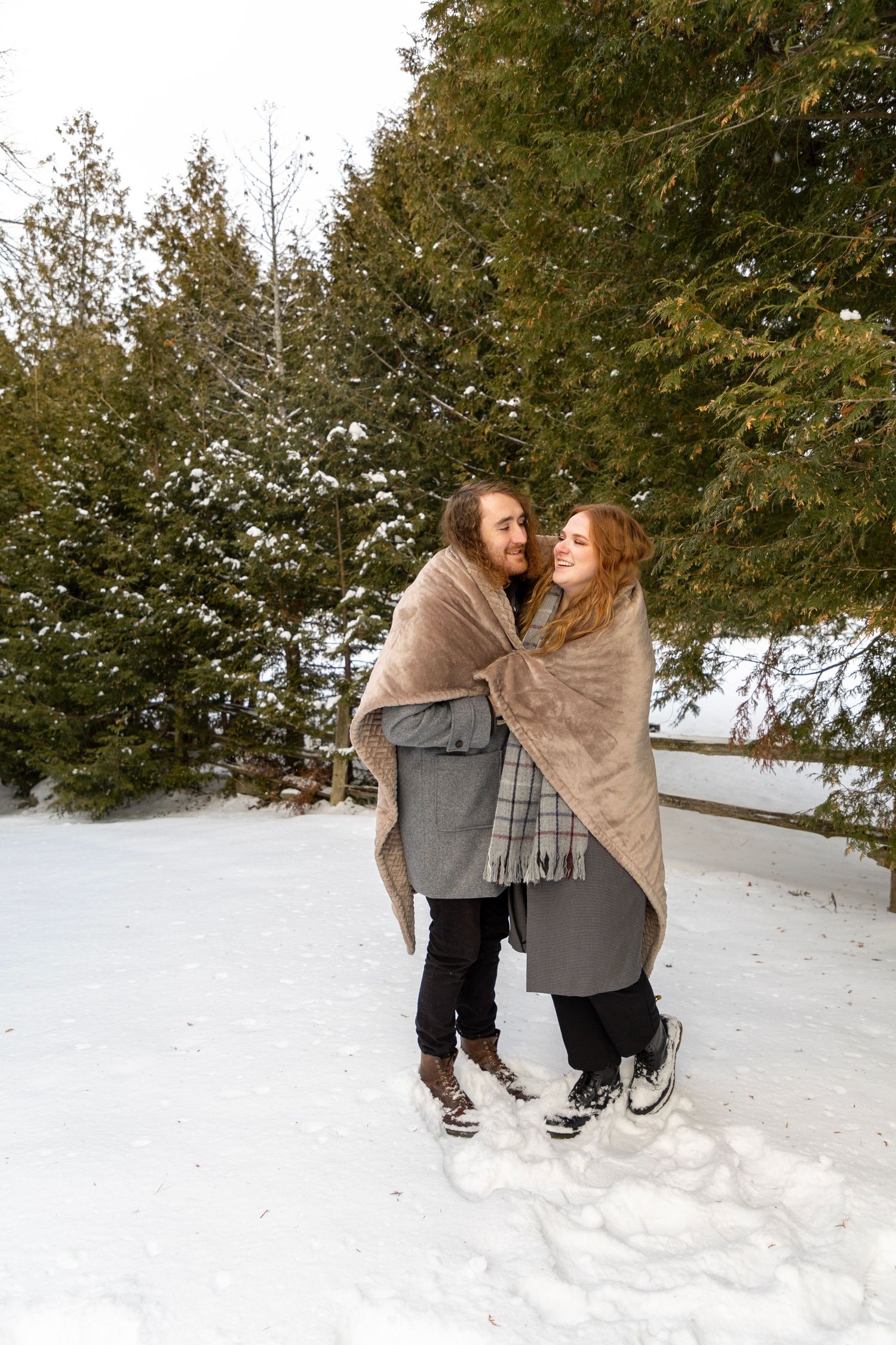 A couple in the winter snow wrapped up in a blanket