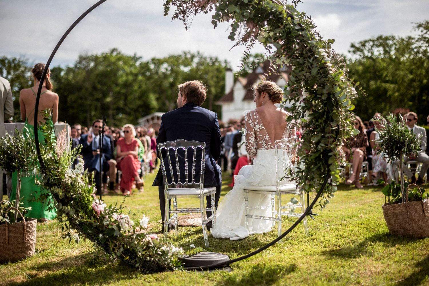 A bride in white dress and groom in navy suit pet horses over a wooden fence with rolling countryside in background.