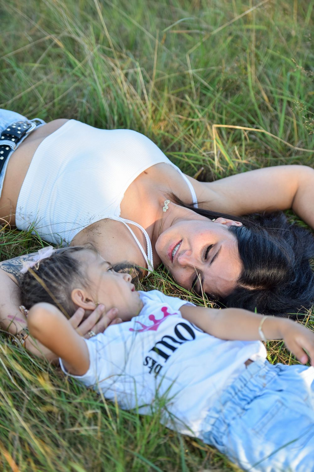 A person in a white top lies peacefully in tall grass during a summer photoshoot.