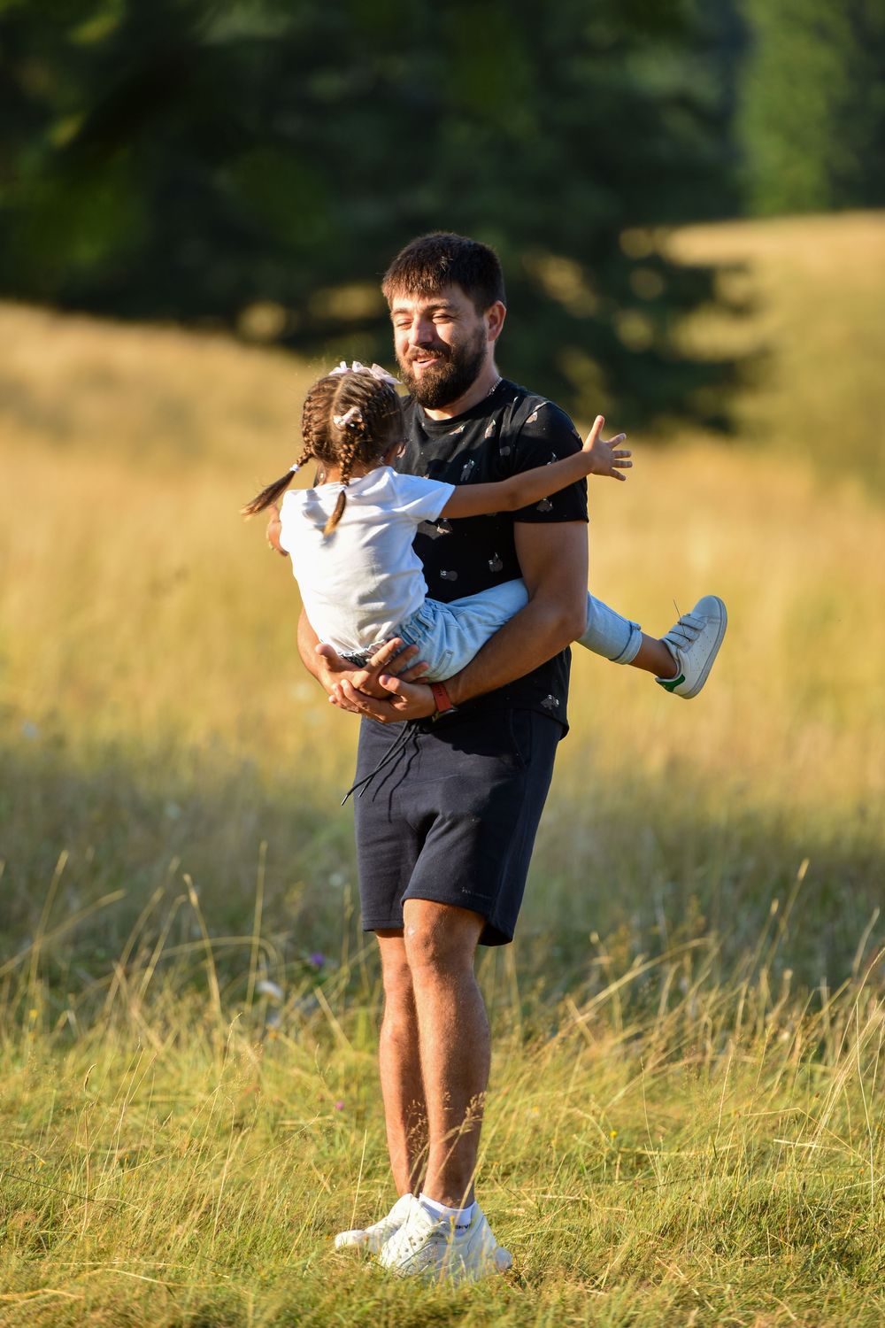 A couple embraces playfully in a sunlit meadow with tall grass during golden hour.