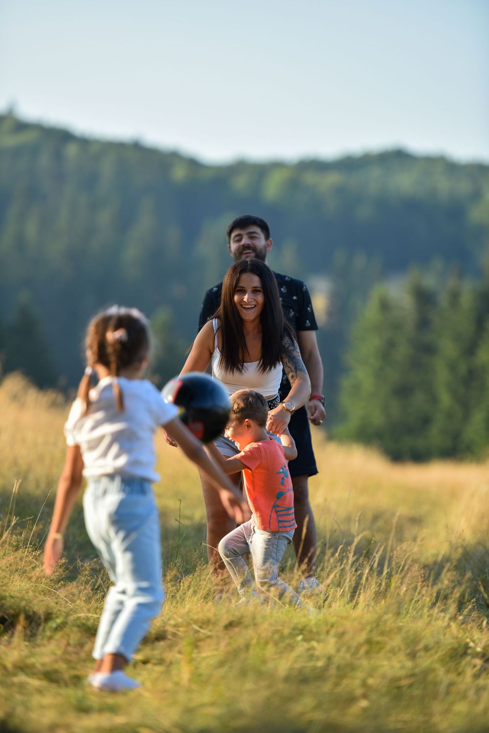 A family enjoys a sunny afternoon walking together through a golden meadow with mountains in the background.