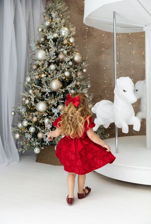 A red dress twirls against a Christmas backdrop with decorated tree and white canopy bed in a festive holiday setting.