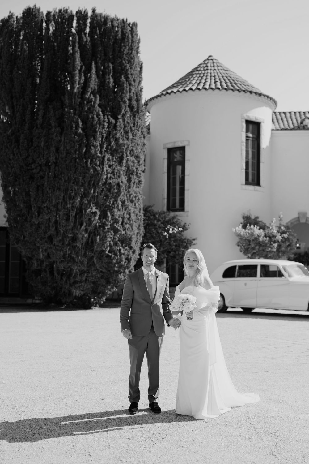 Black and white outdoor wedding photos showing couple and white Mediterranean style building with cypress trees.