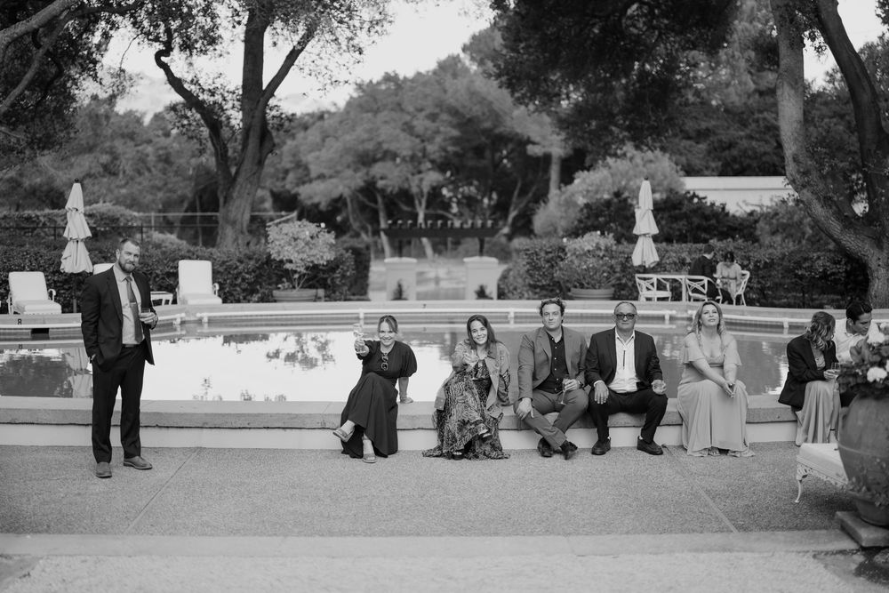 A vintage black and white photograph shows people gathered on steps at a formal outdoor garden with statues.