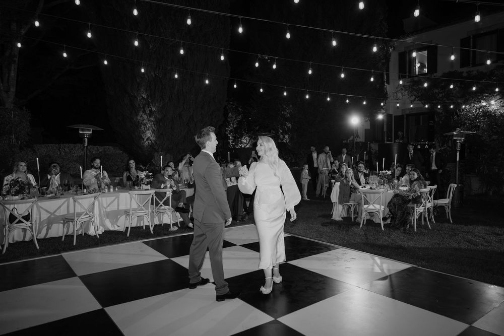 A dark reception venue with a dance floor and twinkling lights overhead illuminating guests dancing at a wedding celebration.