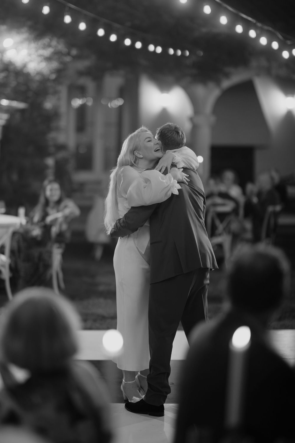 A couple shares a romantic dance under string lights at an evening wedding reception.