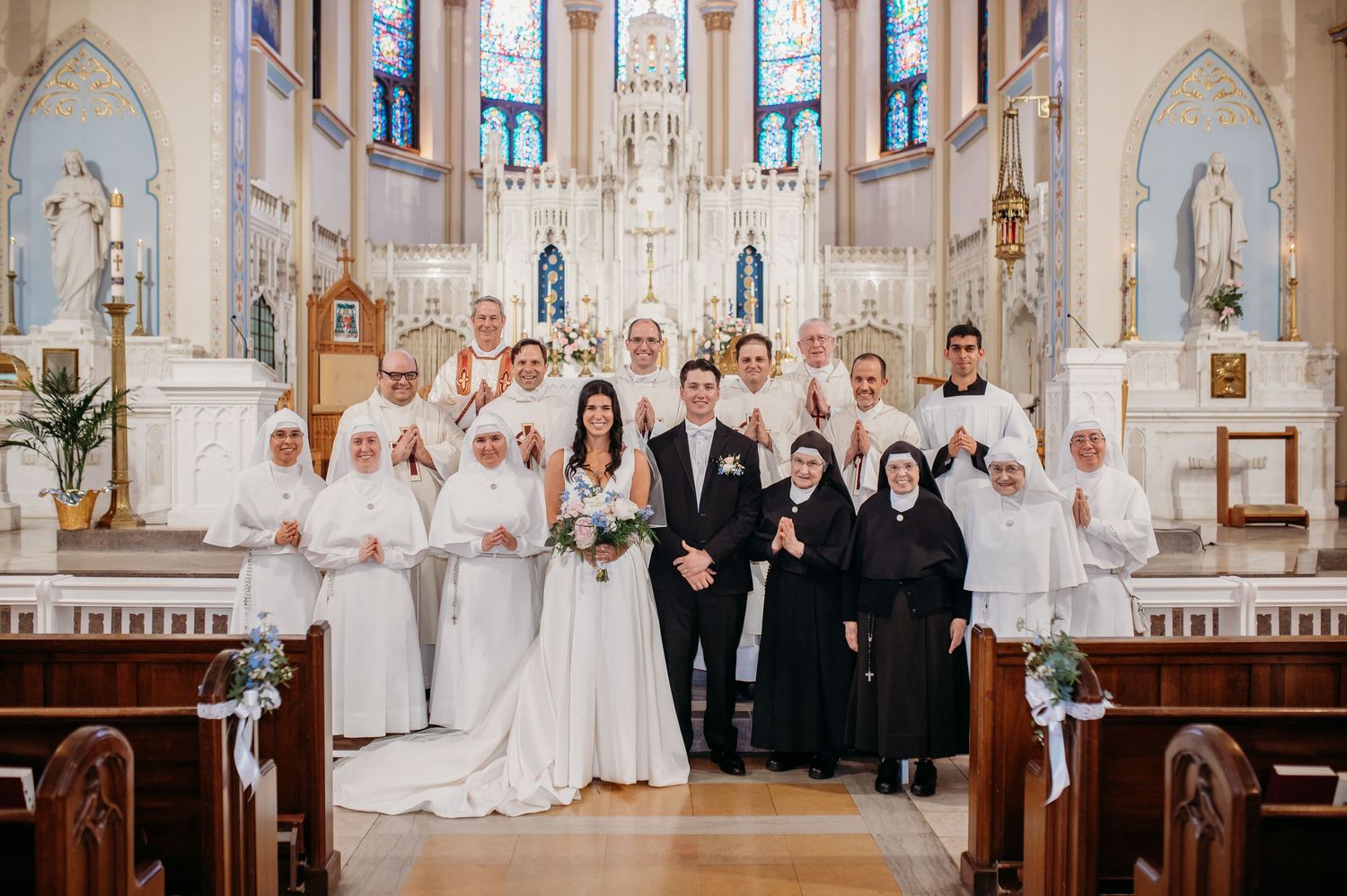 Group of wedding attendees standing together in a beautiful church interior with ornate architecture and stained glass windows.