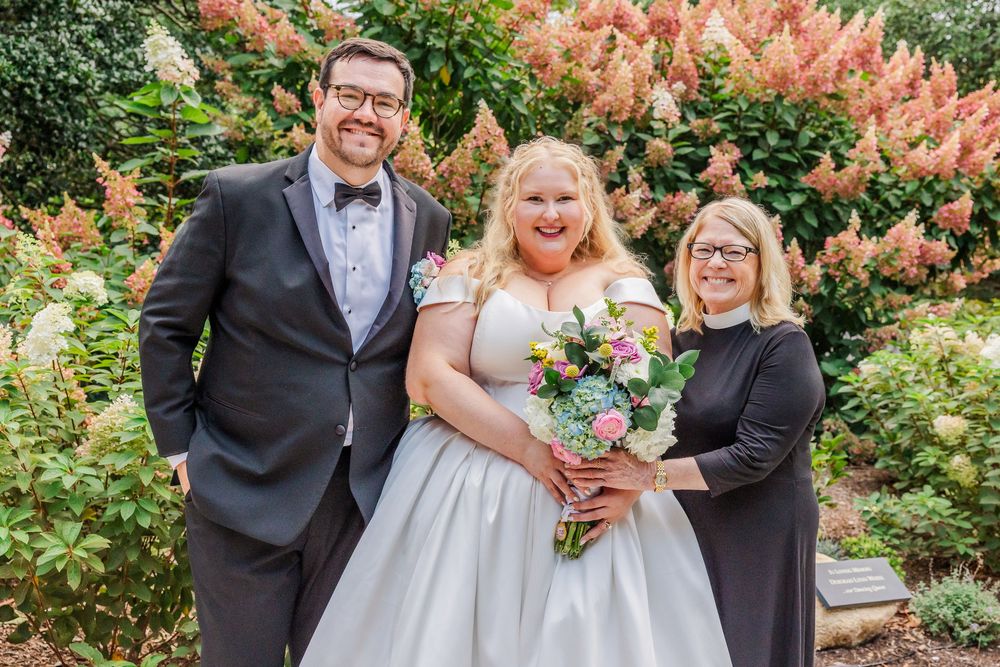 Wedding party poses together in a garden setting with beautiful pink flowering bushes in the background.