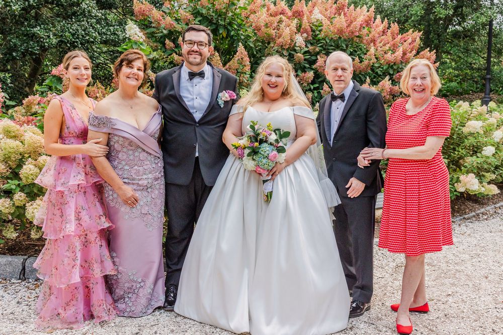 Wedding party poses for formal photos in a garden setting with pink and purple bridesmaid dresses.