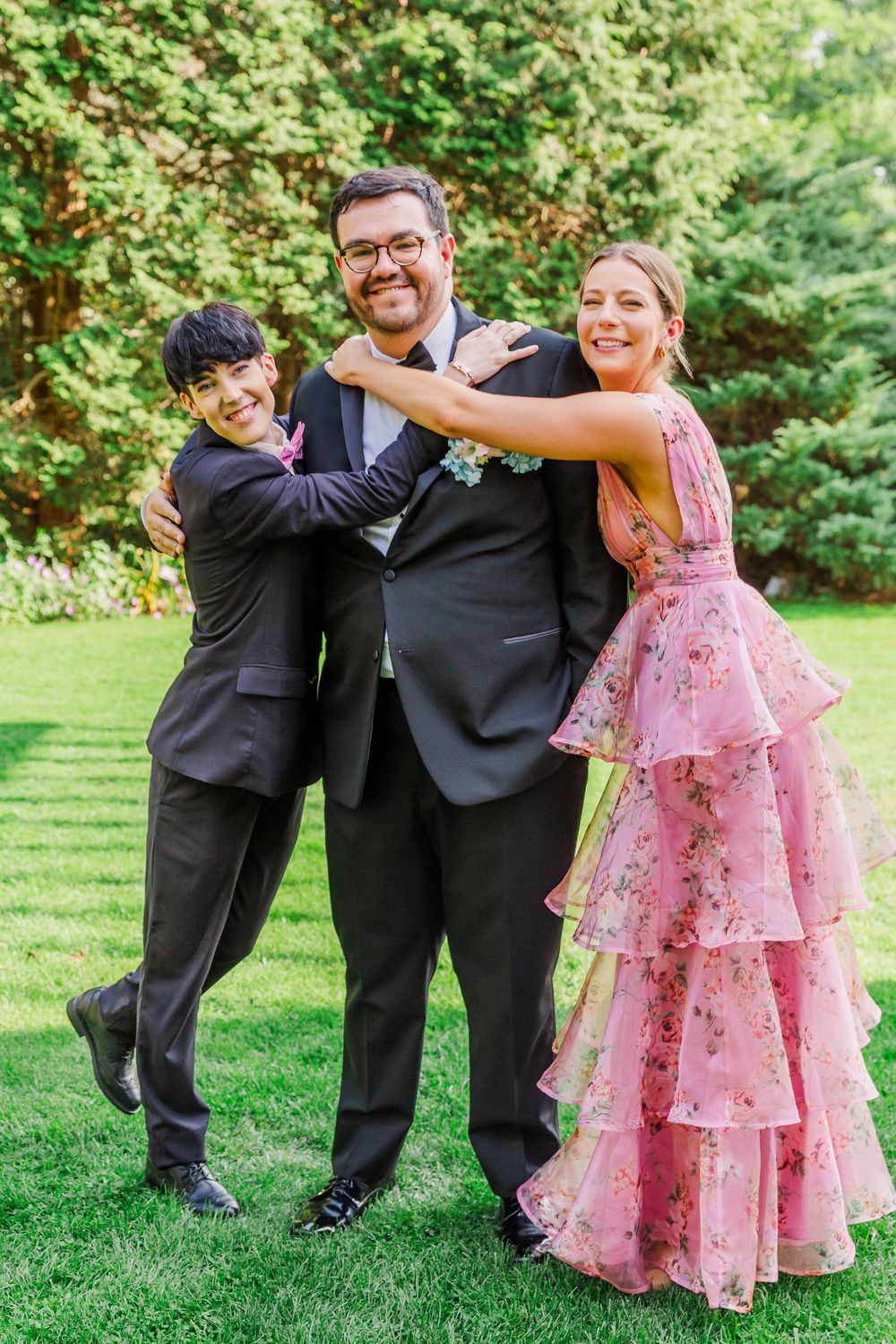 Wedding party members in formal attire share playful moments on a lush green lawn during a summer celebration.