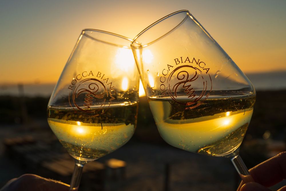 Two wine glasses clinking together against a golden sunset backdrop with vineyard branding visible.